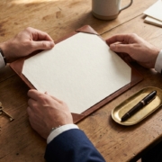 Business-suited Hände prüfen ein Zertifikat in einer Lederdokumentenmappe auf einem Schreibtisch mit Schlüsseln
